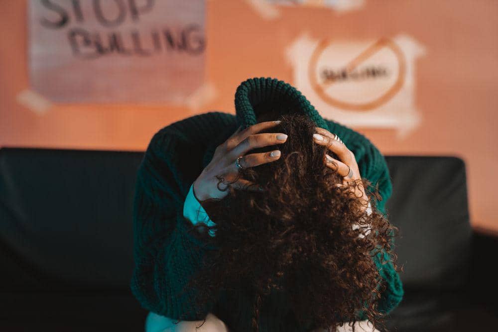 Perempuan terlihat menundukkan kepala dengan tulisan blur Stop Bullying dibelakangnya